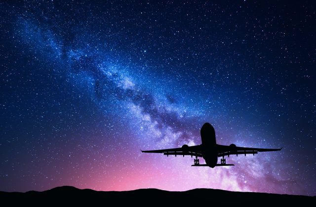 Milky Way and silhouette of a airplane. Landscape with passenger airplane is flying in the starry sky at night. Space background. Landing airliner on the background of colorful Milky Way. Aircraft